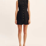 Woman wearing a black sleeveless dress with buttons on a beige background