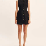 Woman wearing a black sleeveless dress with buttons on a beige background