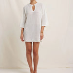 Woman wearing a white crochet dress against a plain background