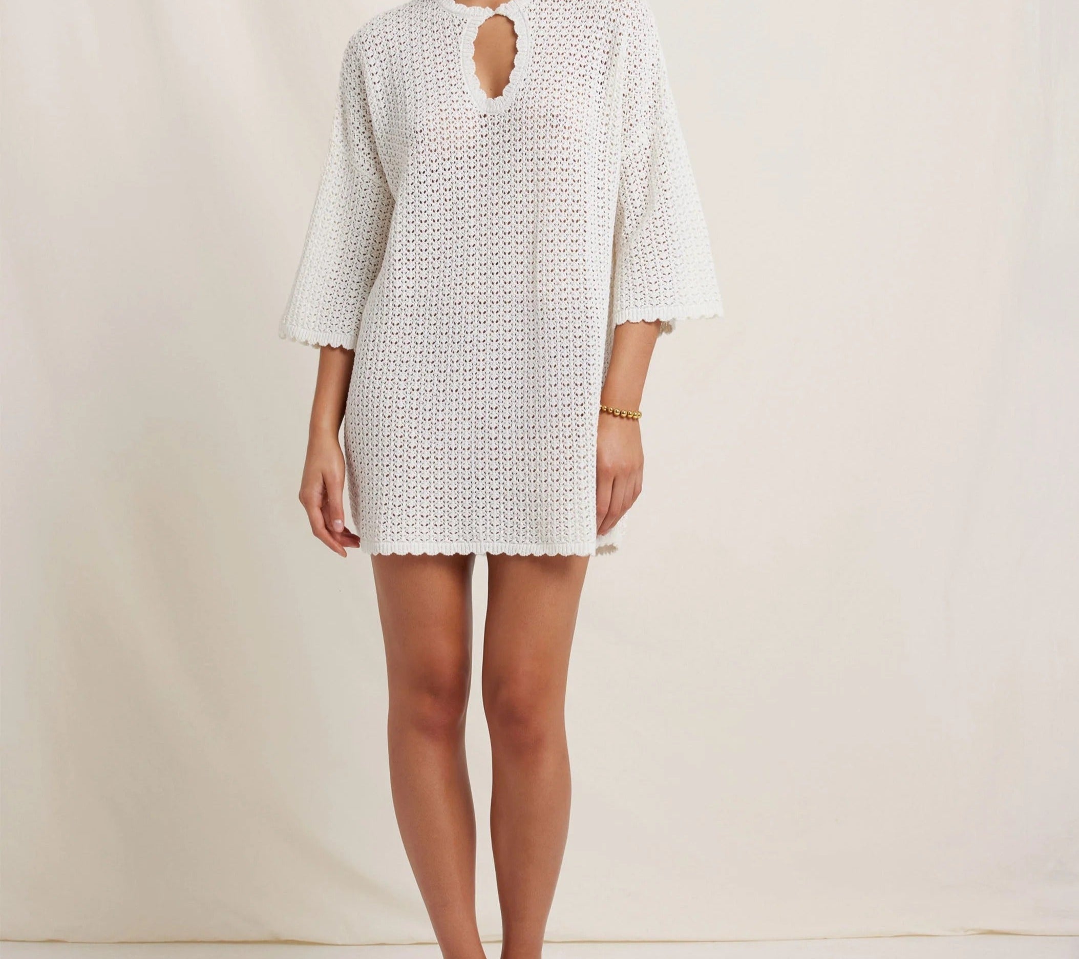 Woman wearing a white crochet dress against a plain background