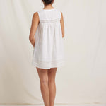 Woman wearing a white sleeveless dress with lace details on a plain background