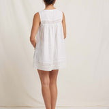 Woman wearing a white sleeveless dress with lace details on a plain background
