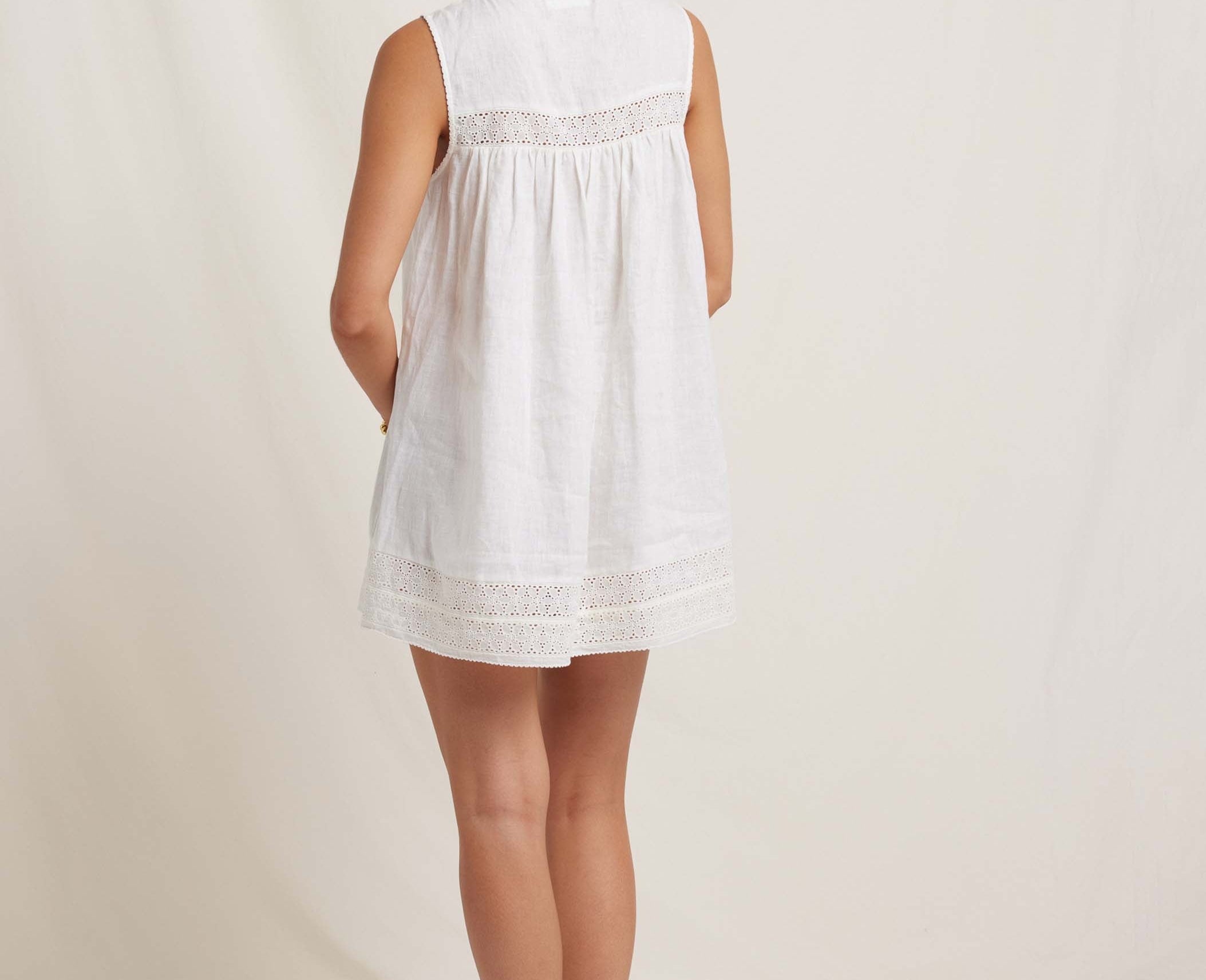 Woman wearing a white sleeveless dress with lace details on a plain background