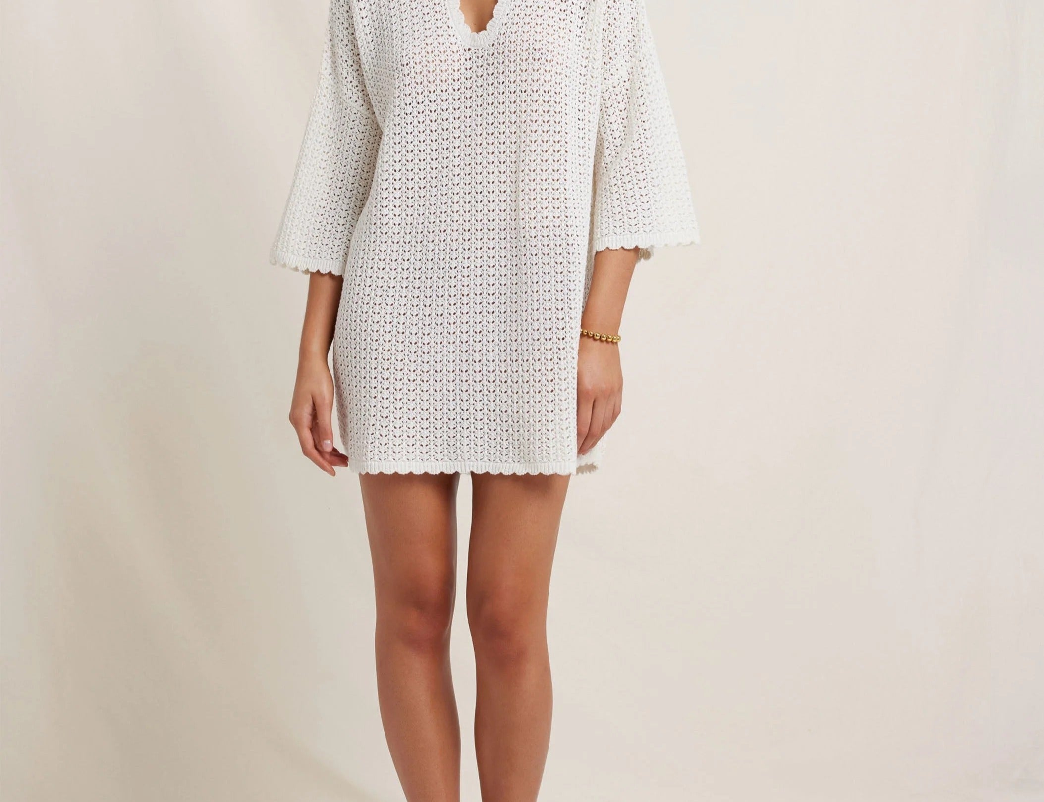 Woman wearing a white crochet dress against a plain background