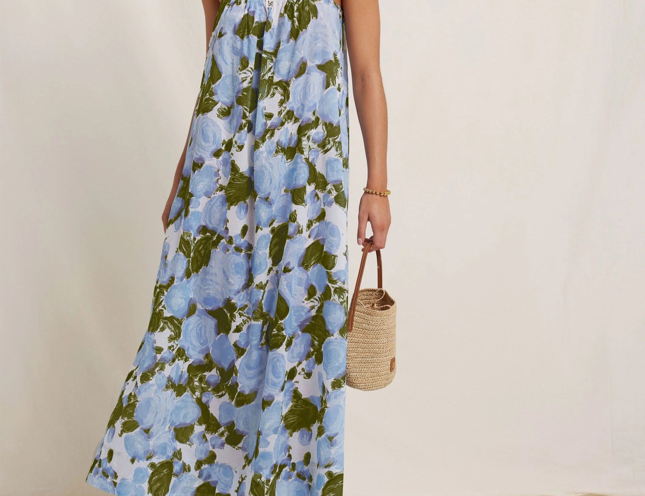 Woman wearing a floral dress holding a woven bag on a plain background