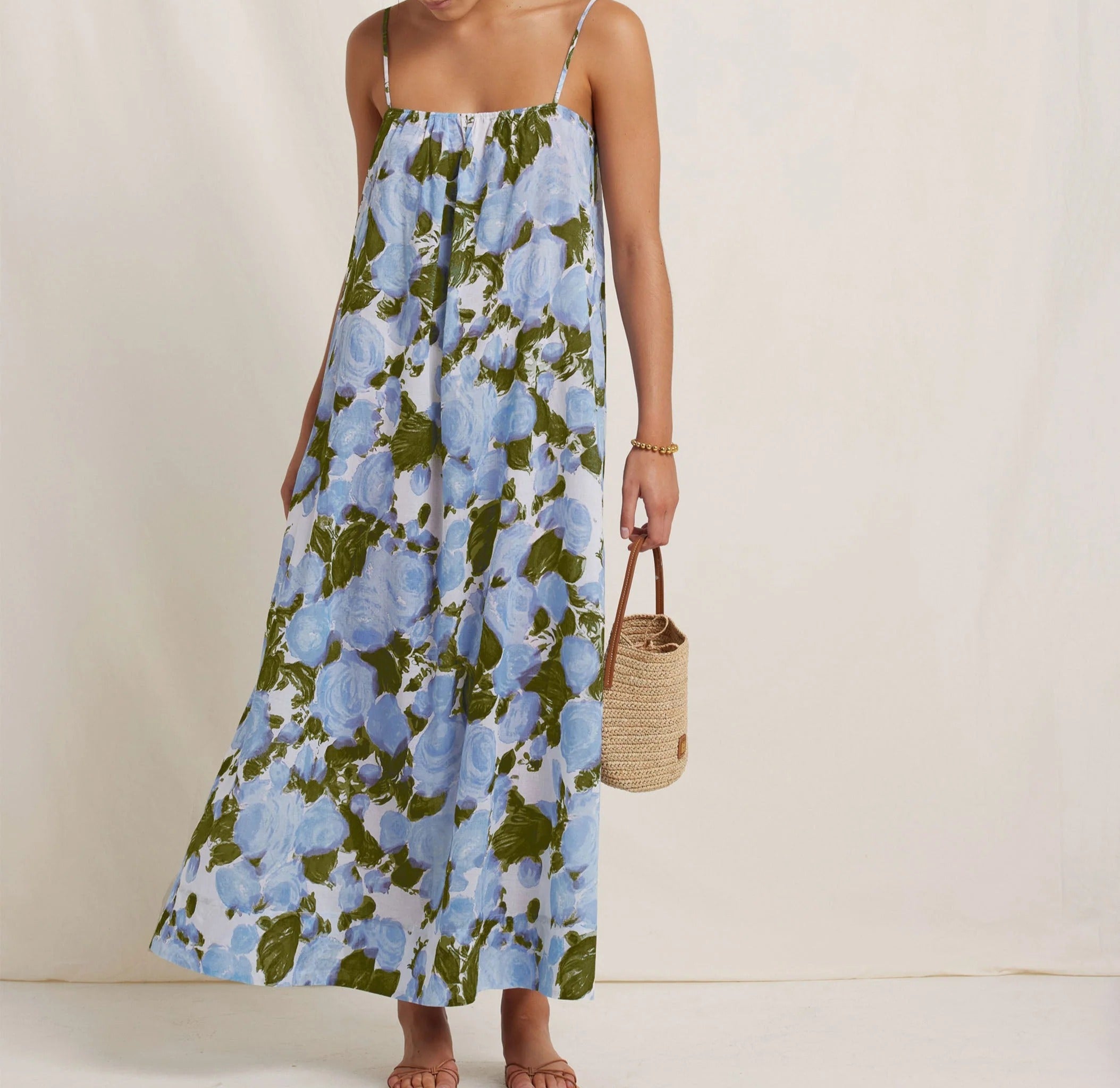 Woman wearing a floral dress holding a woven bag on a plain background