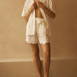Woman wearing a white outfit with lace details against a beige wall