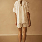 Person wearing a white outfit with lace details against a beige wall