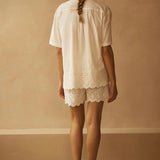 Person wearing a white outfit with lace details against a beige wall