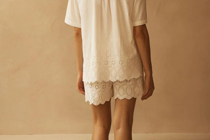 Person wearing a white outfit with lace details against a beige wall