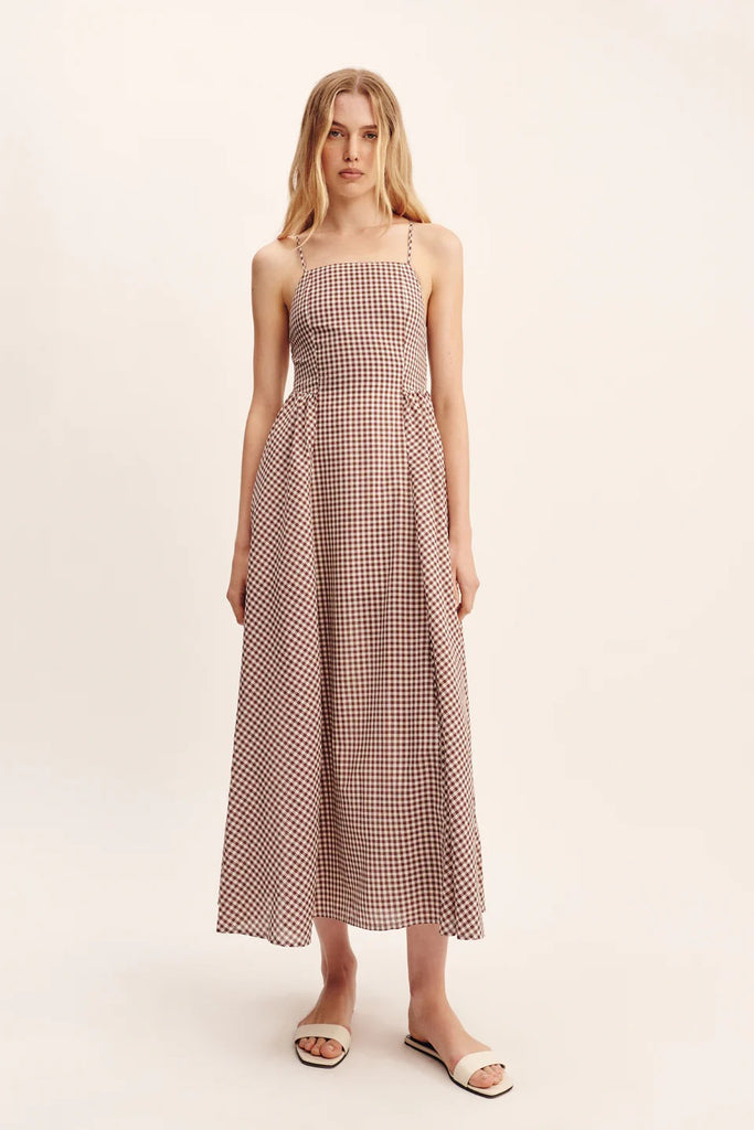 women wearing maxi Dress features a square neckline, elasticated back and free-flowing maxi skirt. It turns to reveal a statement open back with an adjustable tie feature. Mocha Gingham